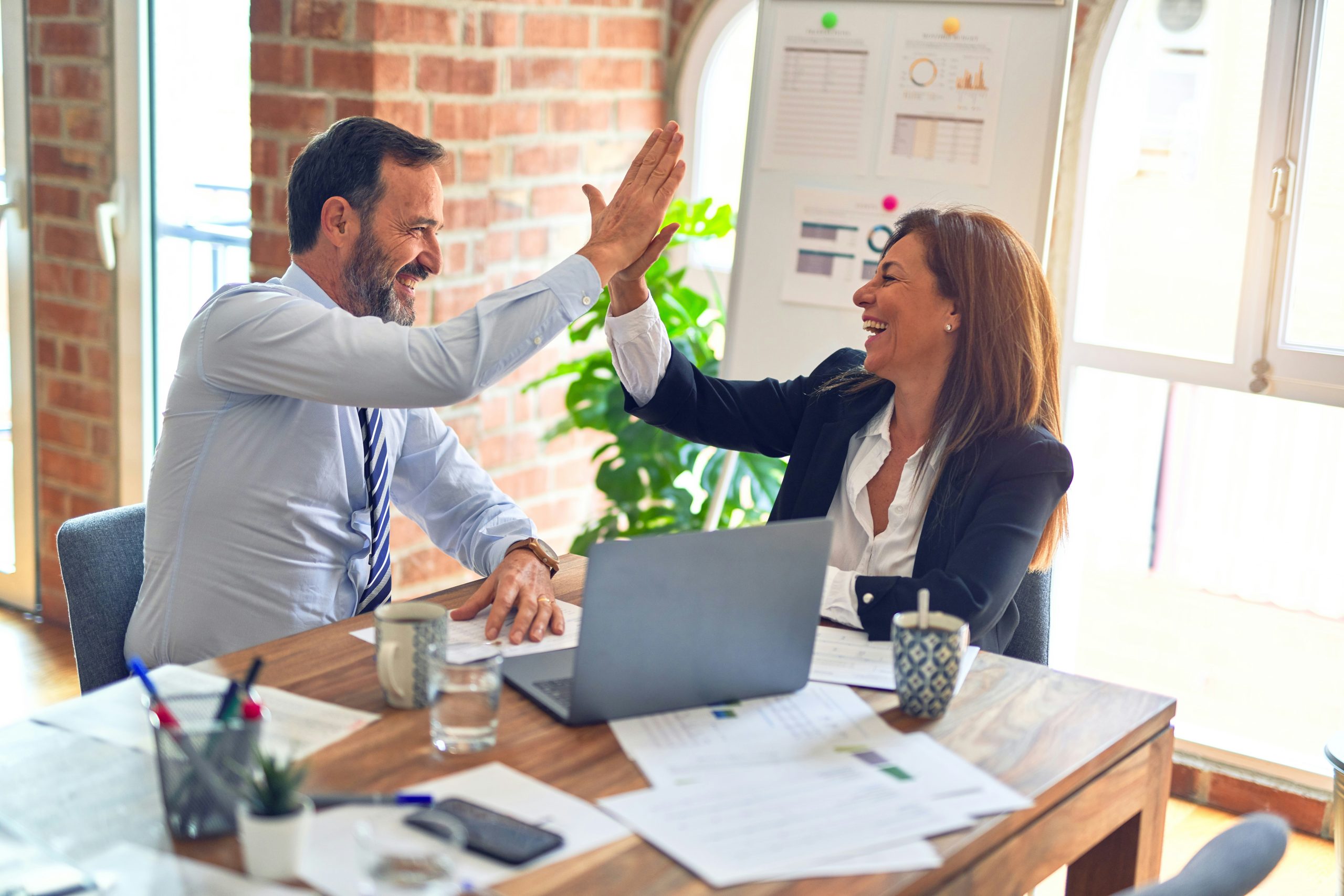 Mann und Frau im Büro feiern Erfolg mit einem High-Five, symbolisieren die positive Dynamik und Ergebnisse durch Beratung in New Leadership und KI-Integration.