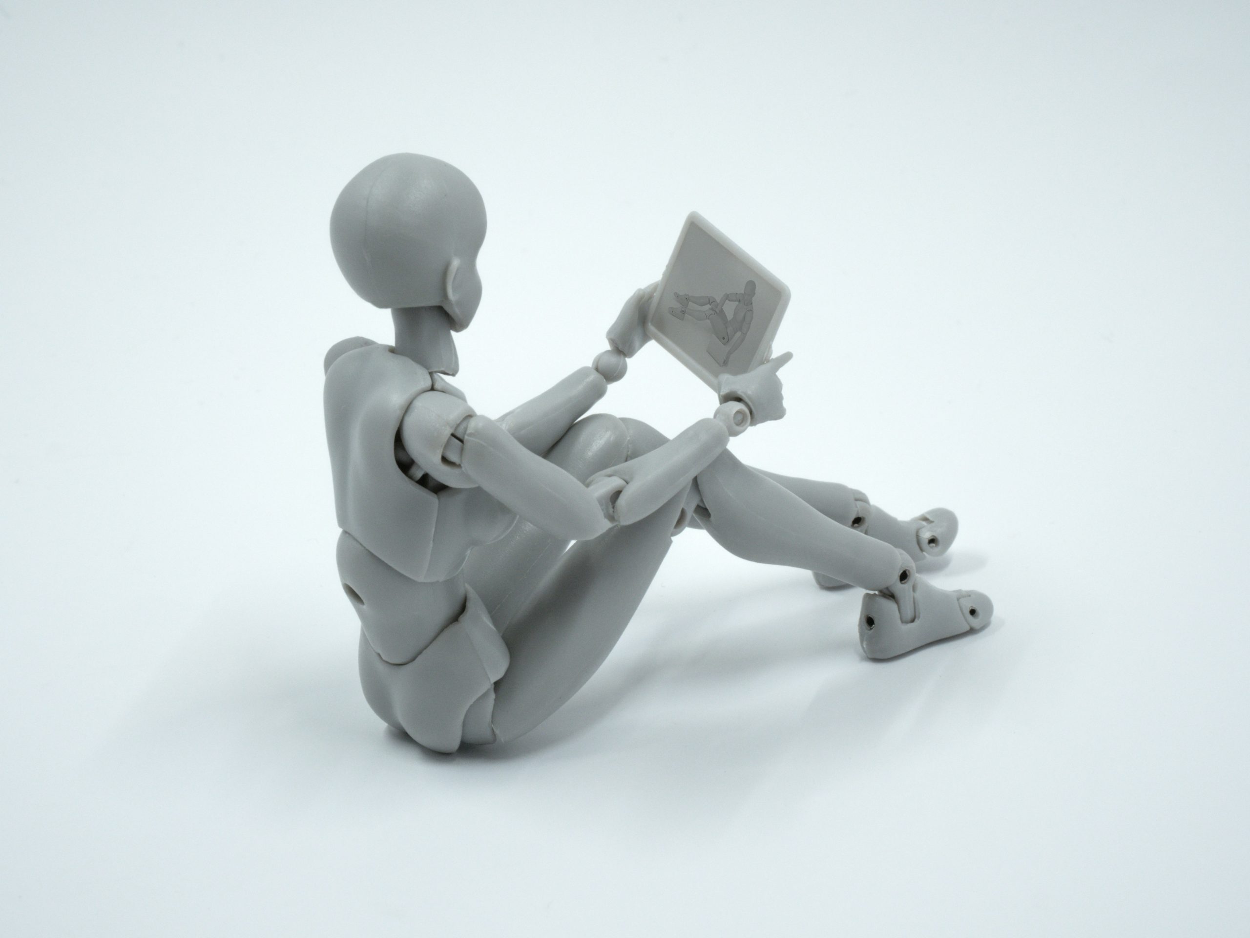Roboter sitzt auf dem Boden und liest auf einem Tablet – Einladung zum kostenlosen Erstgespräch über KI-Integration, symbolisiert das Miteinander-Lernen von Mensch und KI und die Anpassungsfähigkeit von KI-Technologien.